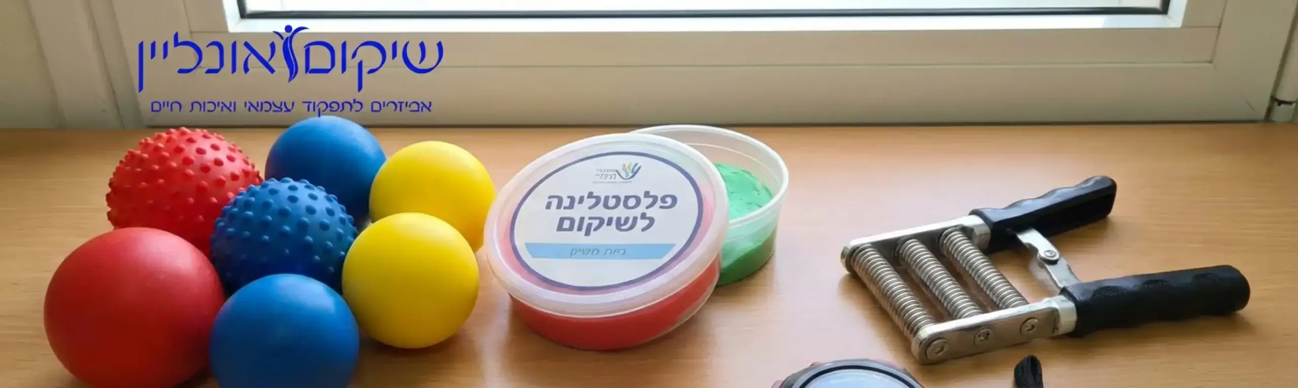 תמונה של שולחן מסודר עם מגוון אביזרי שיקום לכף היד: כדורים צבעוניים, פלסטלינה בקופסה ומכשיר קפיצי, לצד שעון עצר