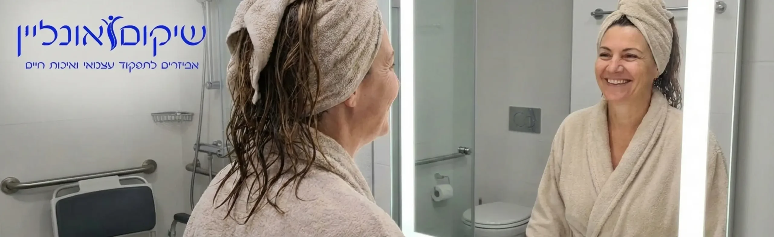 אישה בשנות החמישים לחייה, מביטה במראה בחדר רחצה מואר ונגיש, מחייכת בתחושת הישג לאחר רחצה עצמאית, כשברקע נראה כיסא רחצה מתקדם וידית אחיזה תקנית